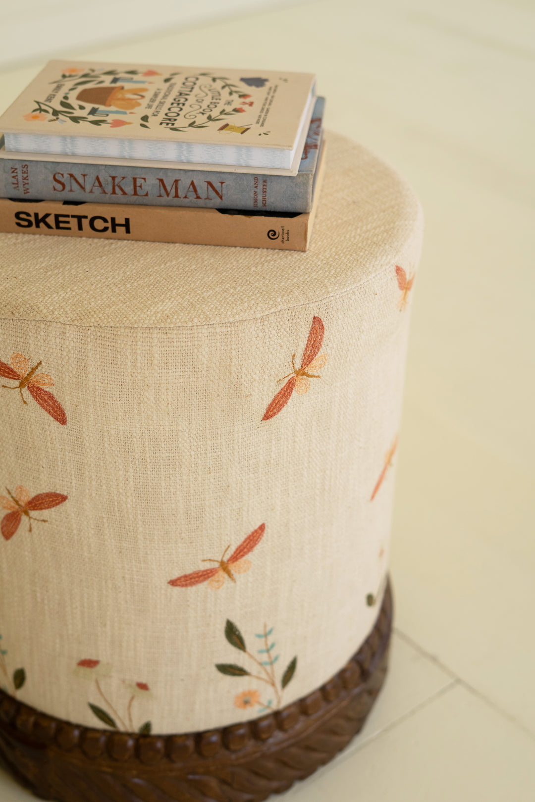 Cream Upholstered Ottoman with Embroidered Detail and Carved Wood Base
