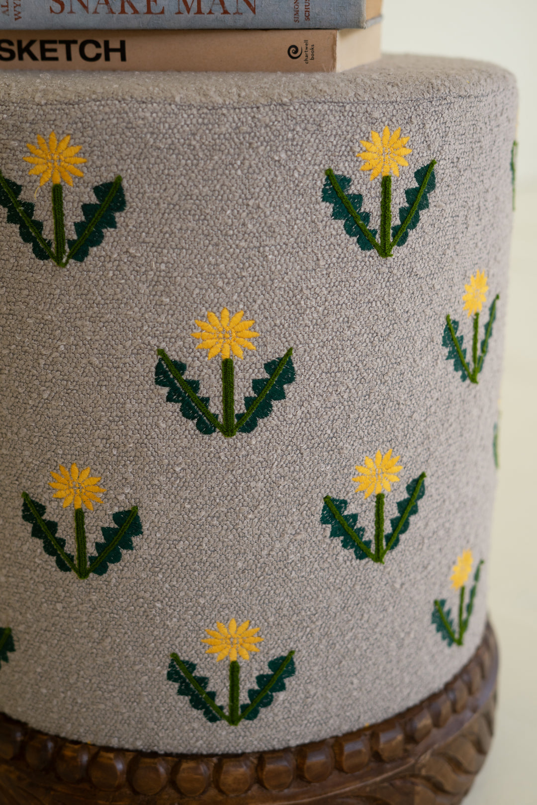 Grey Upholstered Ottoman with Embroidered Detail and Carved Wood Base